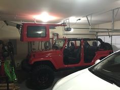 a red jeep parked in a garage next to a white car with its doors open