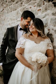 a bride and groom leaning against a stone wall