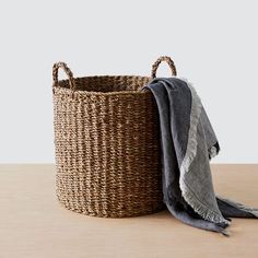 a woven basket with a blanket on top and a gray towel in the corner next to it