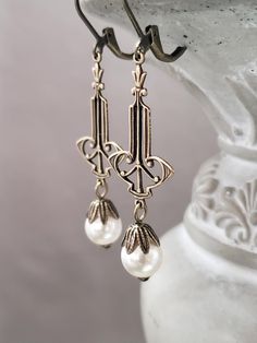 These 1920s inspired pearl dangles feature Deco style dark bronze brass connectors and luminous white glass pearl beads. The lightweight yet sturdy brass connectors are textured on the front and slightly hollow on the back. (SEE 2nd Photo)  These earrings measure 2 1/4 inches long and hang from antique brass lever back ear wires. ABOUT THIS COLLECTION The sophisticated style of the Roaring Twenties is timeless. The sparkling crystal and luminous pearl jewels in this collection are perfect for your 1920s inspired wedding or just your everyday wardrobe. I invite you to browse my complete 1920s Bride Collection here: https://www.etsy.com/shop/BohemeBijou?ref=l2-shopheader-name&section_id=18080838 Vintage Pearl Drop Jewelry For Vintage Events, Wedding Earrings With Antique Finish, Antique Bronze Earrings For Wedding, Victorian Wedding Earrings With Antique Finish, Vintage Wedding Earrings With Antique Finish, Vintage Wedding Pearl Earrings, Vintage Metal Pearl Earrings For Wedding, Elegant Brass Earrings With Antique Finish, Elegant Brass Jewelry For Vintage Events