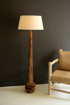 a wooden lamp sitting next to a chair in a room with a dark wall behind it