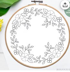 a cross stitch pattern with flowers and leaves in the hoop on a white table next to yellow flowers