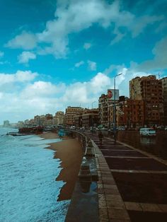 people are walking along the beach next to the water and buildings on either side of the ocean