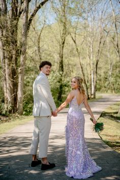 a bride and groom holding hands while standing on a path in front of some trees