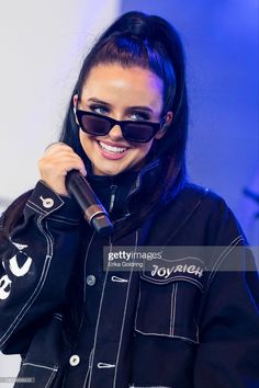 a woman in black jacket and sunglasses holding a microphone