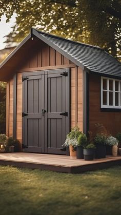 a small wooden shed sitting on top of a grass covered field with potted plants