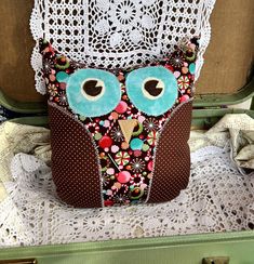 an owl pillow sitting on top of a lace doily covered table cloth next to a suitcase