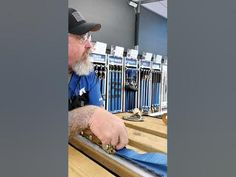 an older man is making something out of blue material on a wooden table in a room with metal railings