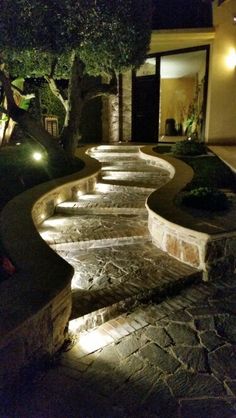 an outdoor walkway lit up at night in front of a house with trees and bushes