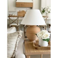 a table with a lamp on top of it and flowers in a vase next to it