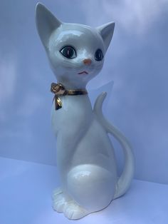 a white cat figurine with blue eyes and a gold bow around its neck