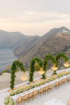 an outdoor dining area with tables and chairs overlooking the ocean, surrounded by greenery