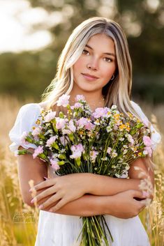 a woman in a white dress holding a bouquet of pink and yellow flowers with her arms crossed