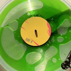 a person is holding scissors in a green bowl with water and bubbles on it that has a yellow disc attached to the bottom