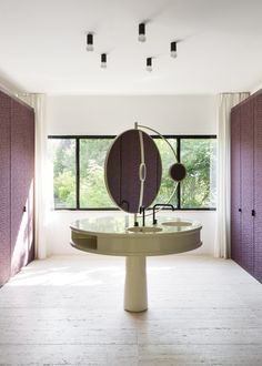 a room with purple walls and white flooring has a round mirror on the table