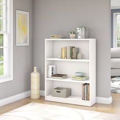 a white book shelf with books on top of it next to a window in a living room