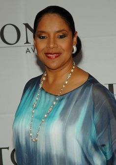 a woman in a blue and green dress smiling at the camera with pearls on her necklace