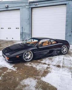 a black sports car parked in front of a garage door with snow on the ground