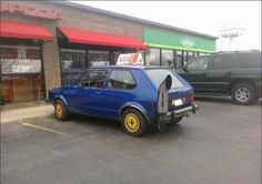 a small blue car parked in front of a building next to a parking lot with other cars