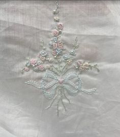 an embroidered white fabric with pink and blue flowers on it's side, along with a bow in the center