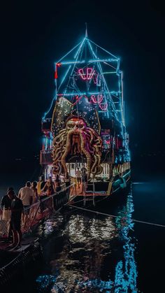 people are standing on the dock watching an octopus float in the water at night time