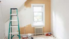 an empty room with a ladder, window and painting supplies on the floor in front of it