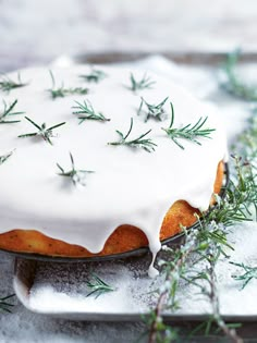 a frosted cake sitting on top of a pan covered in green sprigs