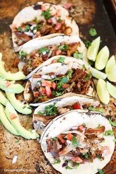 several tacos are lined up on a baking sheet with avocado wedges