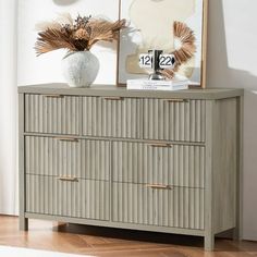 a dresser with two vases on top of it next to a clock and pictures