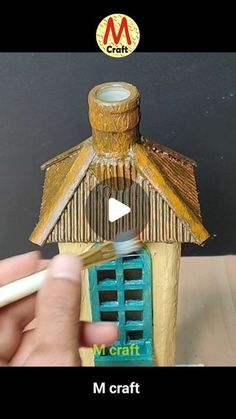 a person holding a pencil in front of a miniature house