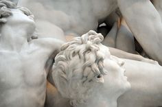 two white marble statues with one laying on his back and the other standing behind him