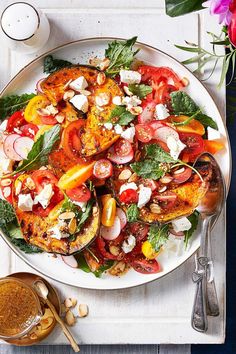 a white plate topped with lots of food next to a bowl of sauce and spoons