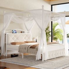 a white canopy bed sitting on top of a wooden floor