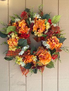 an orange and red wreath hanging on the side of a white building with flowers in it