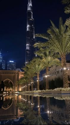 the burj building is lit up at night with palm trees in front of it