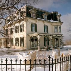 a large white house sitting on top of a snow covered field next to a tree