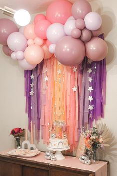 a table topped with lots of balloons next to a wall filled with streamers and stars