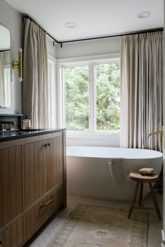 a bath tub sitting next to a window in a bathroom under a vanity and mirror