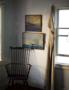 a chair sitting in front of a window next to two paintings on the wall and a lamp