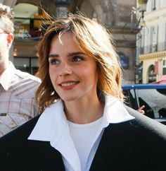 a woman in black and white jacket walking down the street with another man behind her