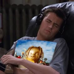 a man laying in a chair with headphones on and holding a painting that looks like a golden buddha