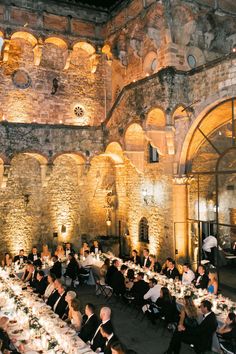 a large group of people sitting at tables in a room with stone walls and arches