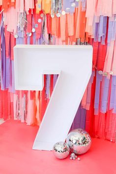 a large number seven sitting next to two balls on a pink floor with streamers in the background