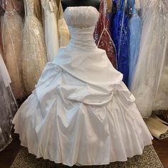 a white wedding dress sitting on top of a wooden floor next to other gowns