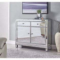 a silver mirrored cabinet in a living room next to a white chair and vase on the floor