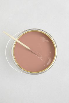 a pink paint in a bowl with a wooden stick sticking out of the top, on a white surface