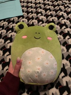 a hand holding a green frog pillow on top of a black and white patterned blanket