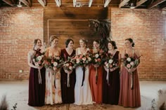 a group of women standing next to each other in front of a brick wall holding bouquets