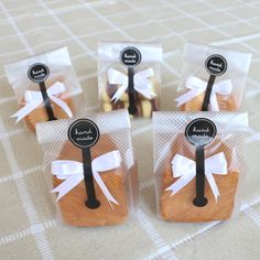 four packaged cookies in cellophane bags with white bows and black labels on them