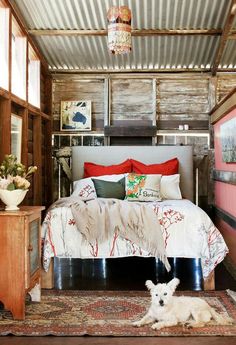 a dog laying on the floor in front of a bed with red and white pillows